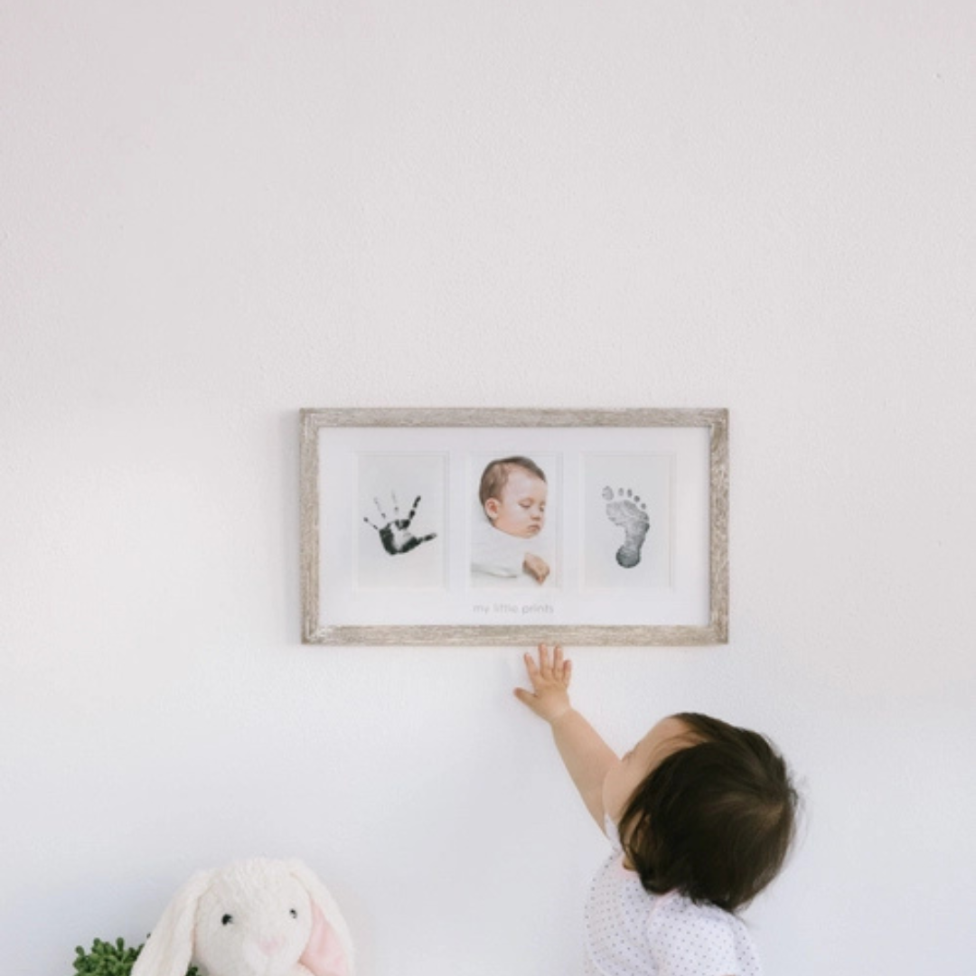 Rustic wooden baby handprint and footprint frame hanging on a nursery wall beside soft neutral décor.