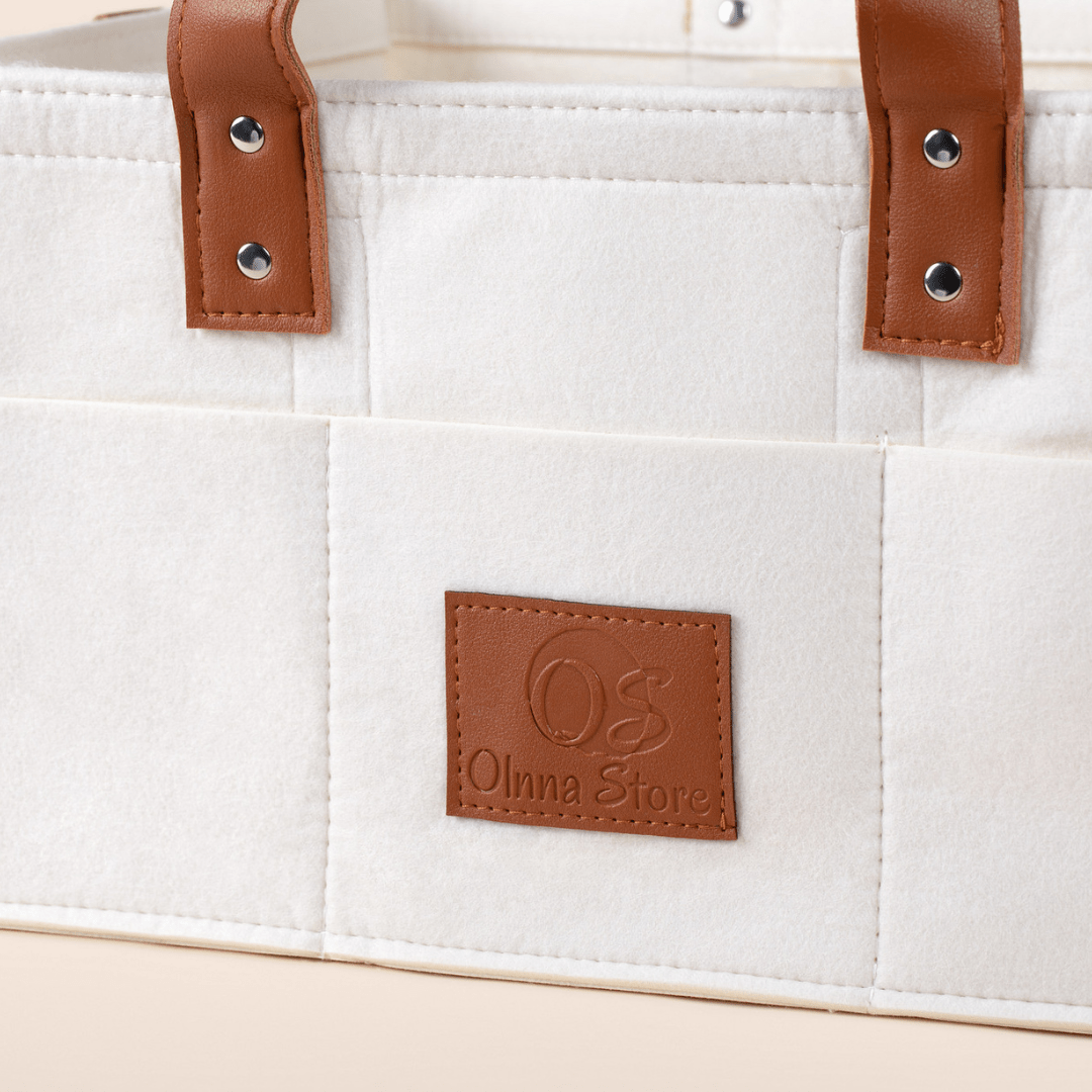 Cream tote bag with brown leather handles and a brand label on a white background