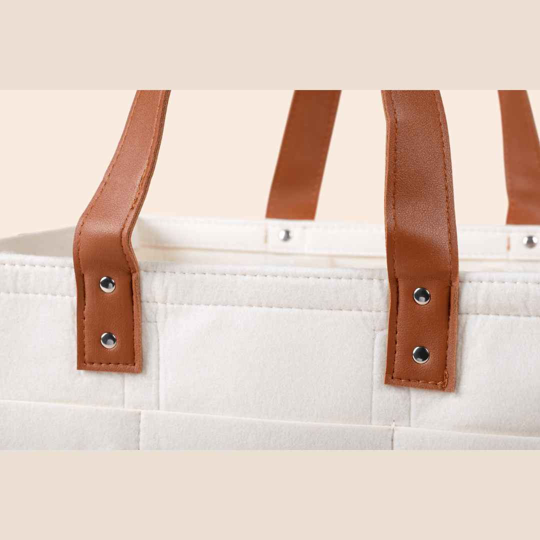 Cream tote bag with brown straps and decorative buttons on a beige background