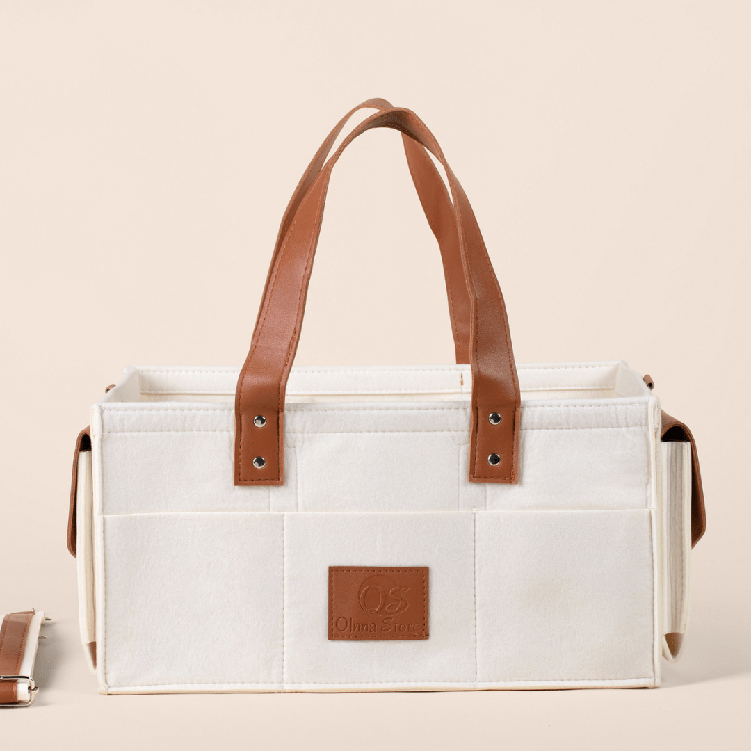 Cream tote bag with brown leather handles and accents on a beige background