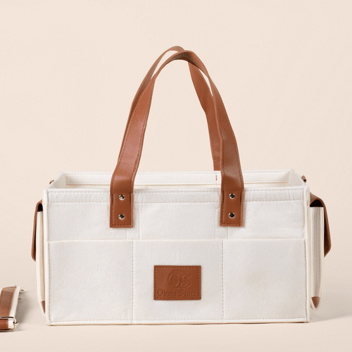 Cream tote bag with brown leather handles and accents on a beige background